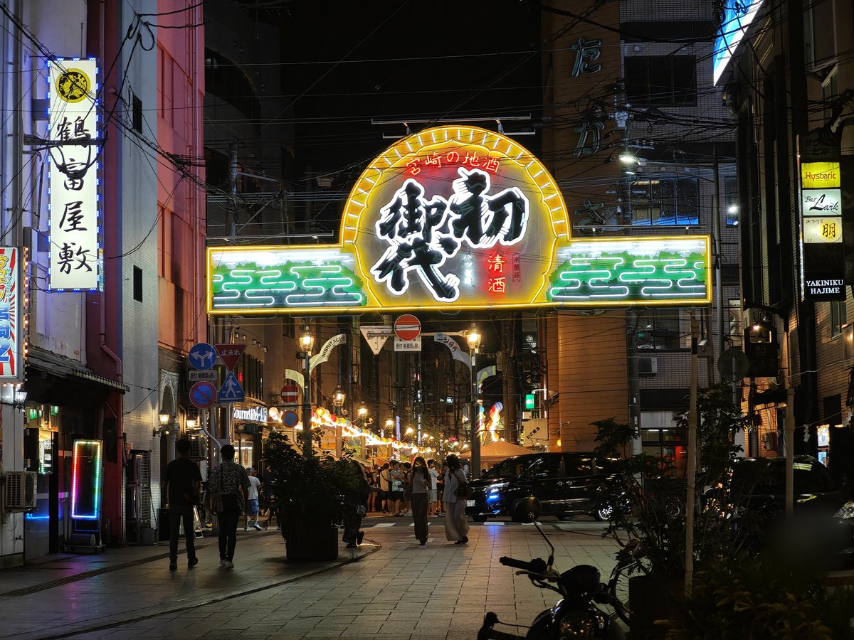 夜の繁華街の通りと、光る門形の看板